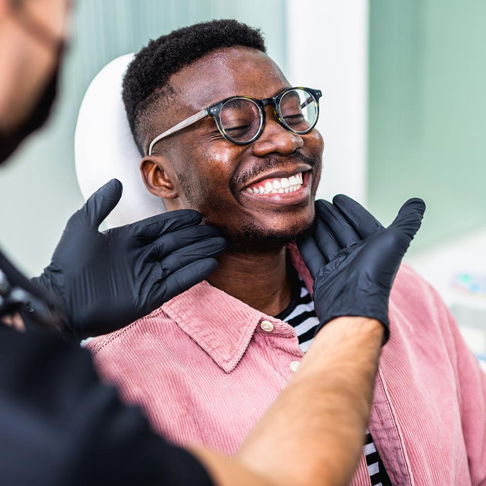 A man seated in a barber chair with a broad smile, receiving a haircut from a barber who appears to be focused on his work.