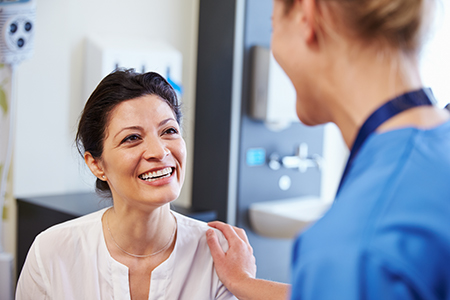 The image shows two people in a medical setting one person appears to be a patient receiving care from another who is likely a healthcare professional, with both individuals smiling and engaging in an interaction that suggests a positive experience.